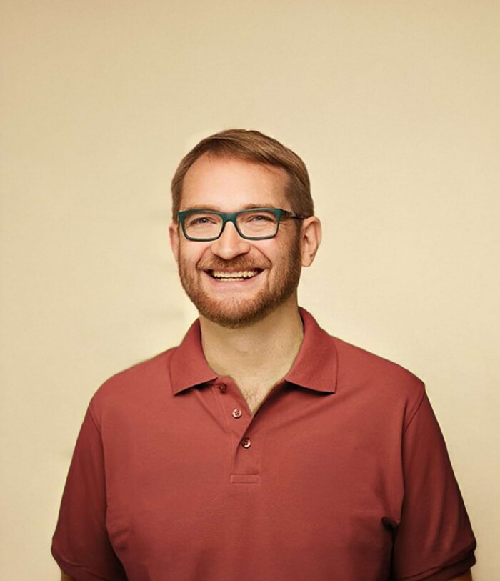 Freundliches Portrait von Dr. Ermark in einem bordeauxroten Polo, vor warmweißem Hintergrund – Kinderarzt in Landau