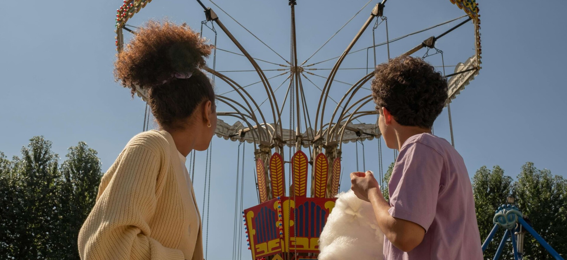 Zwei Kinder stehen vor einem Ketten-Karussell und schauen es gespannt an.