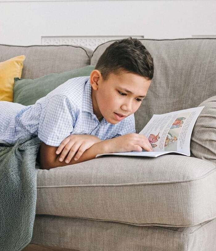 Ein Junge liegt auf dem Sofa und liest in einem Buch.