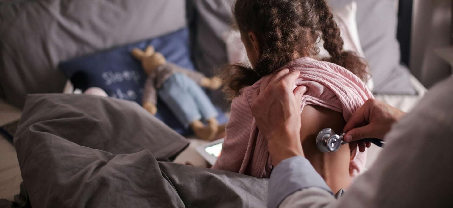 Ein Mädchen sitzt mit dem Rücken zum Arzt und wird mit einem Stethoskop am Rücken abgehört.