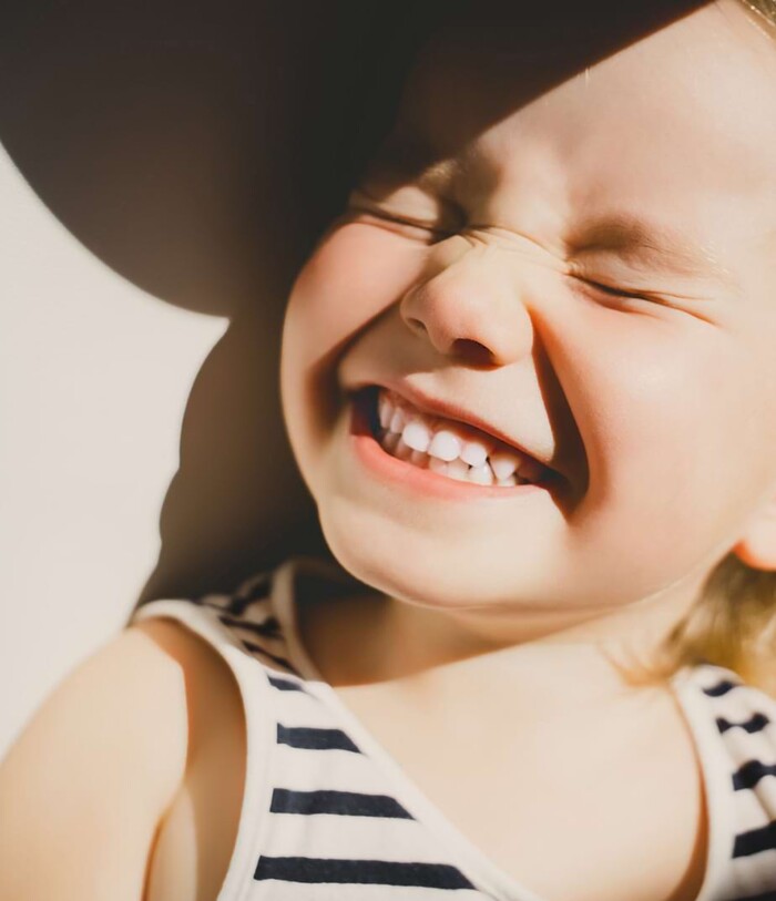 Ein goldiges kleines Mädchen lehnt an der Wand und grinst frech in die Sonne.