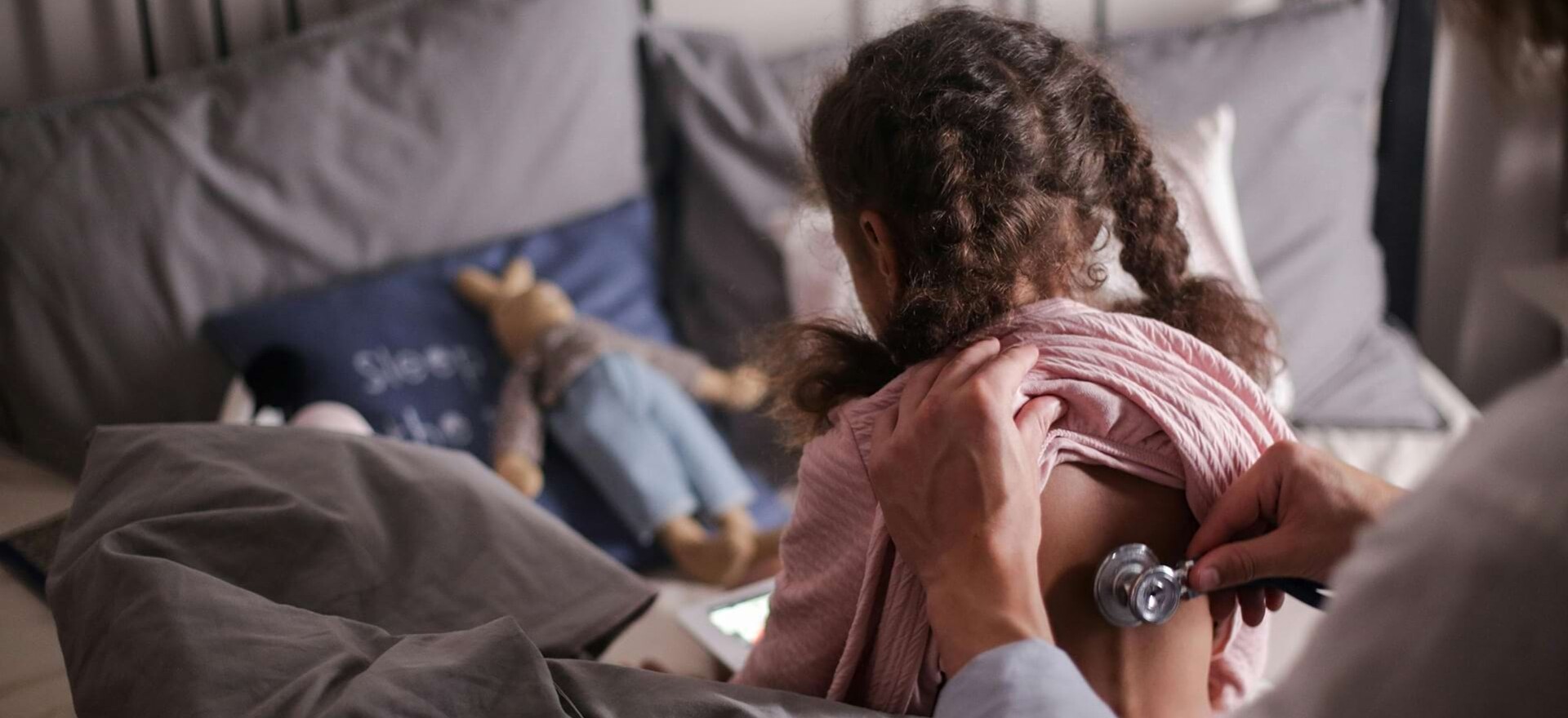 Ein Mädchen sitzt mit dem Rücken zum Arzt und wird mit einem Stethoskop am Rücken abgehört.
